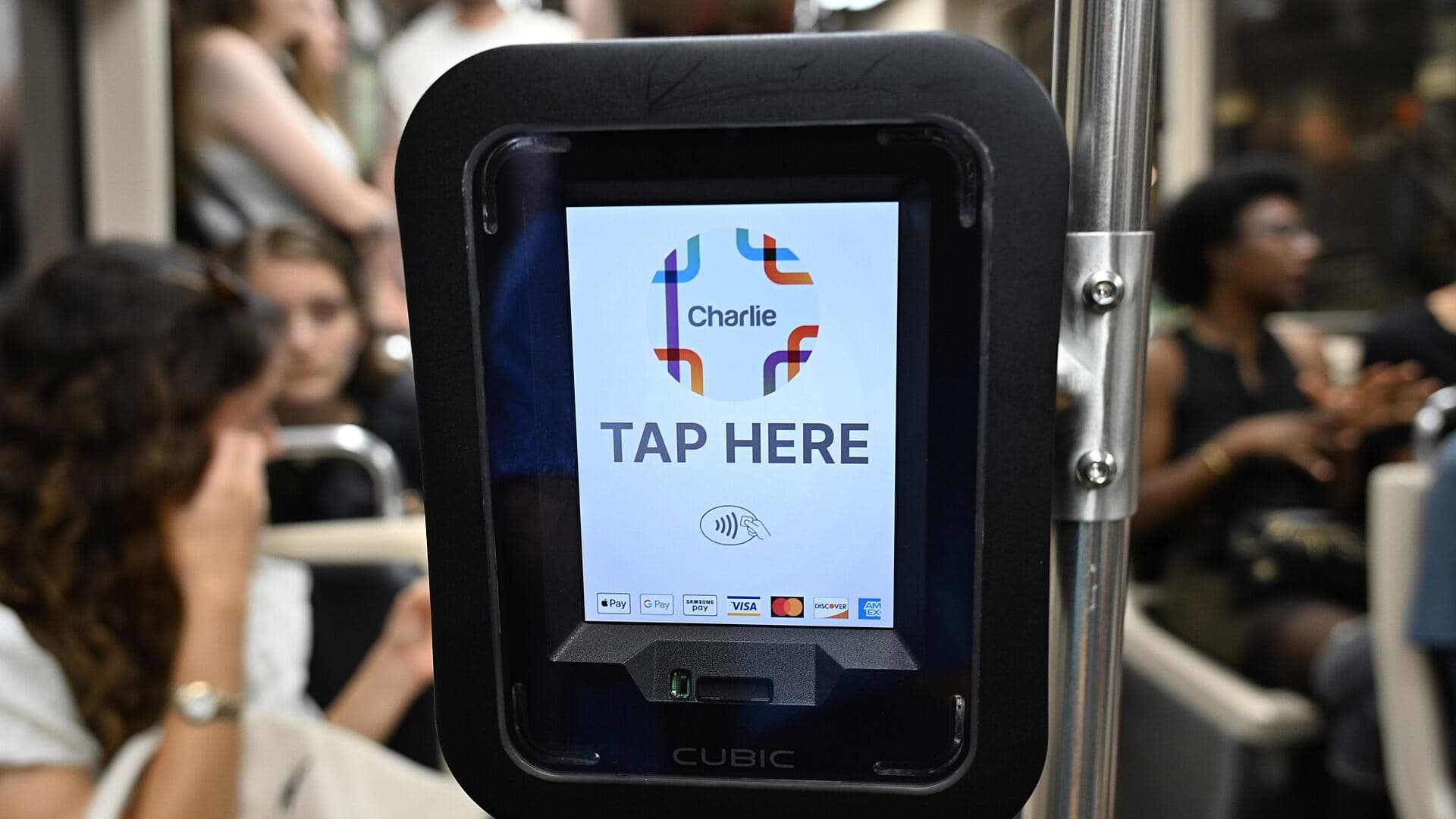A contactless fare reader mounted inside a tram carriage, passengers seated behind it