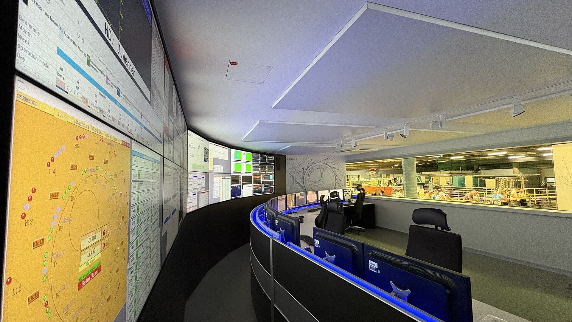 A large operations control room, banks of consoles facing a wall of screens
